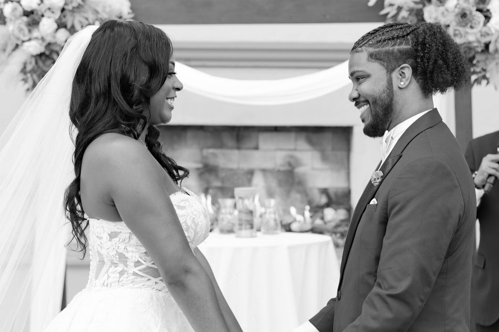 A bride and groom share a joyful moment during their wedding ceremony in a black and white photo.