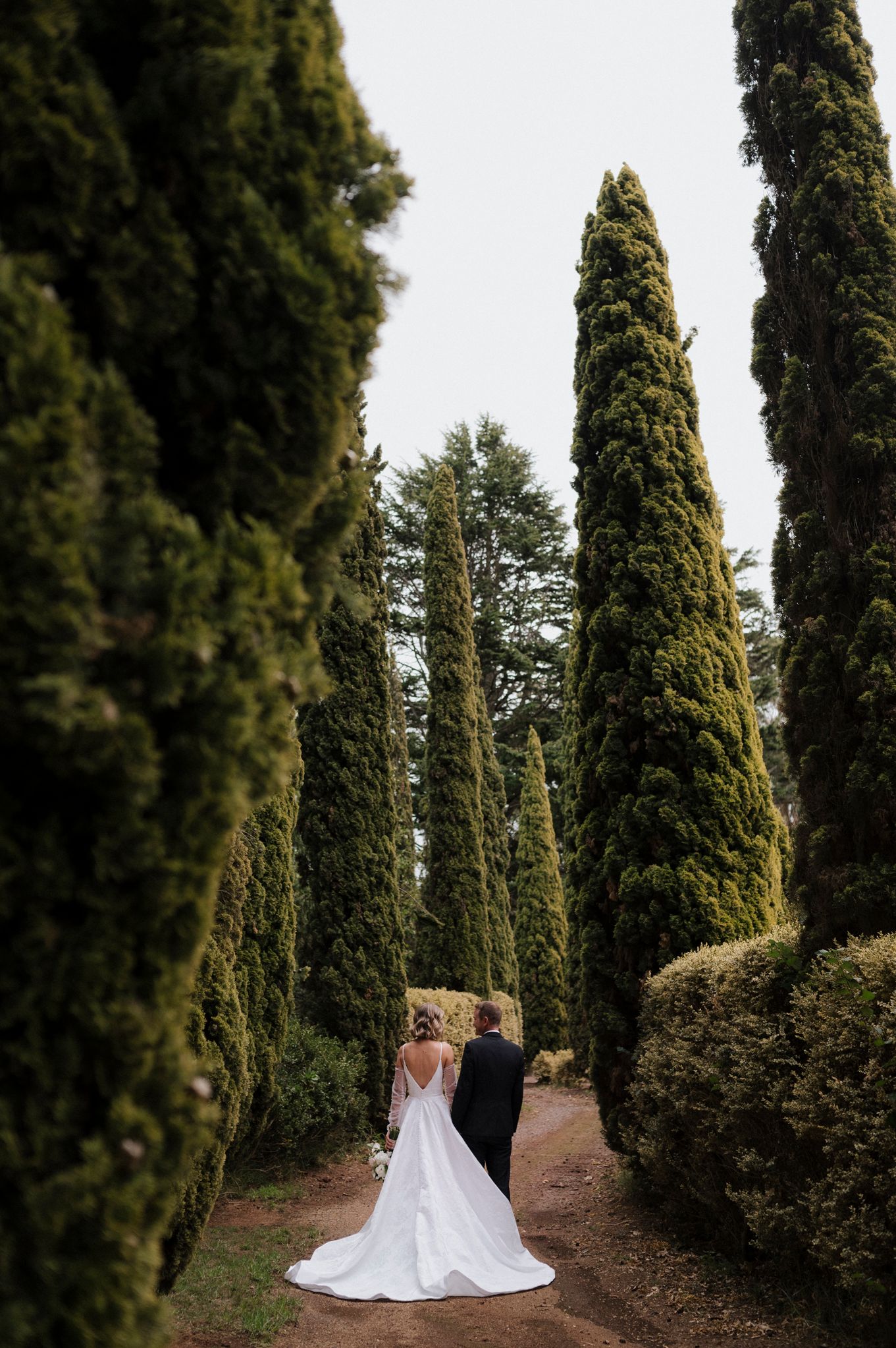 Black and white wedding photo of bride and groom standing under ornate iron gazebo arch in formal garden.