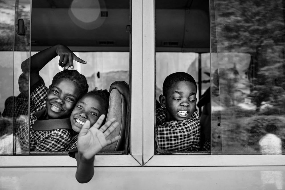 Black and white photo of three joyful children waving and smiling from a bus window.