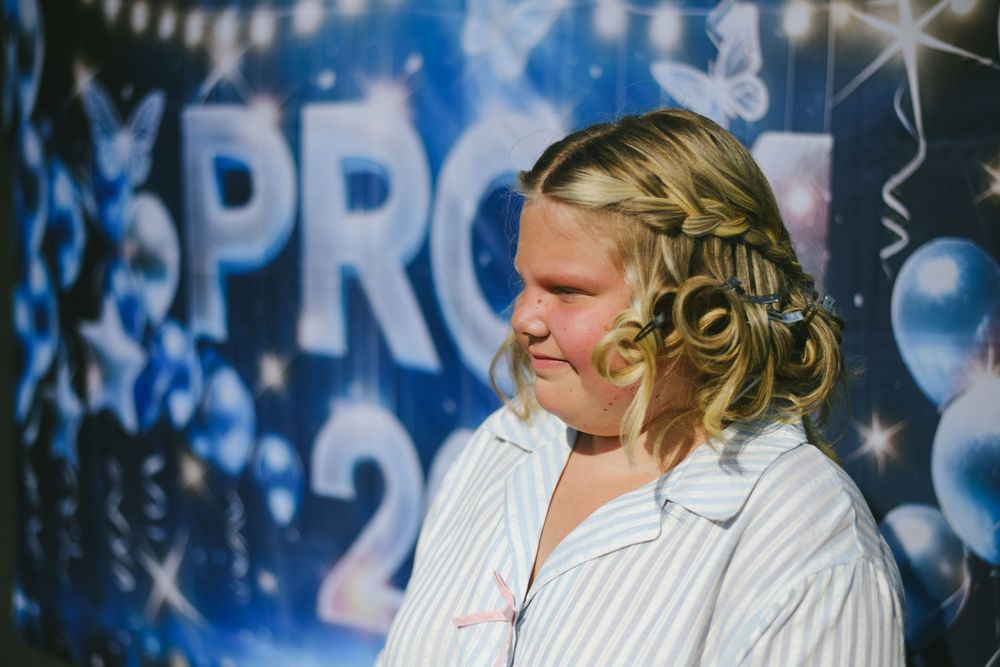 Young woman with braided updo hairstyle smiling in front of blue prom backdrop.