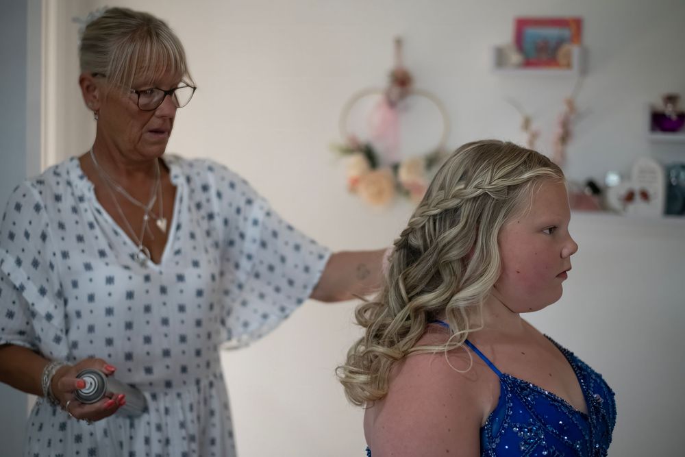 Older woman helping young girl in blue sequin dress with hair preparation for a formal event.