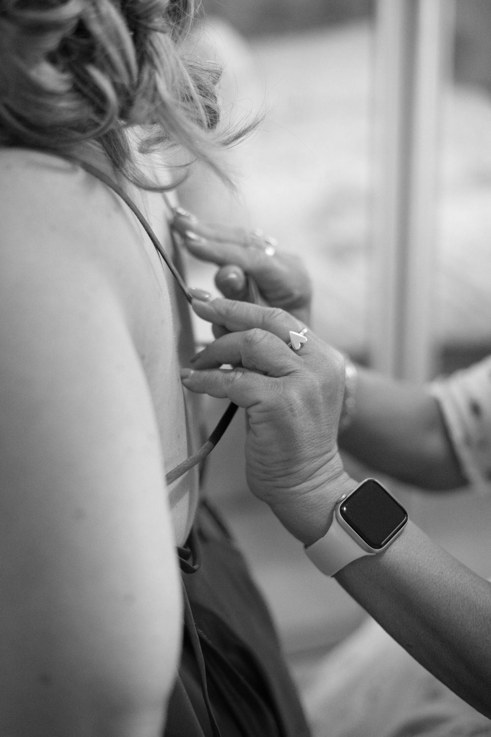 Black and white photo of hands fastening a wedding dress, one wearing an Apple Watch and diamond ring.