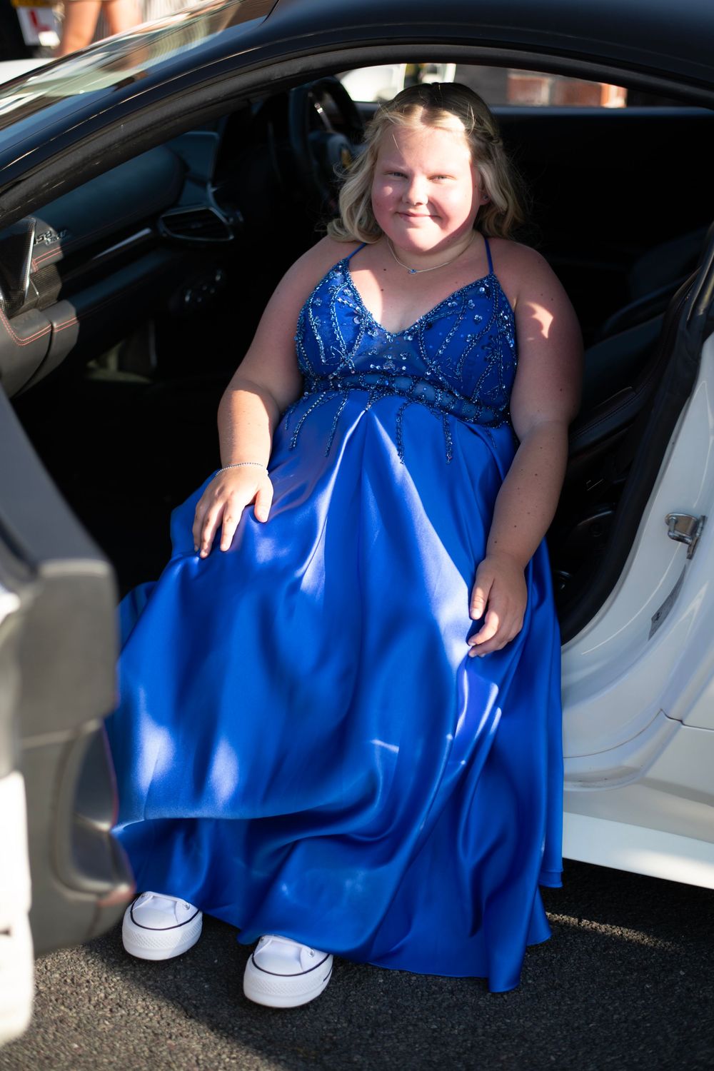 Young girl in blue sequined prom dress stepping out of a white car, wearing white sneakers.