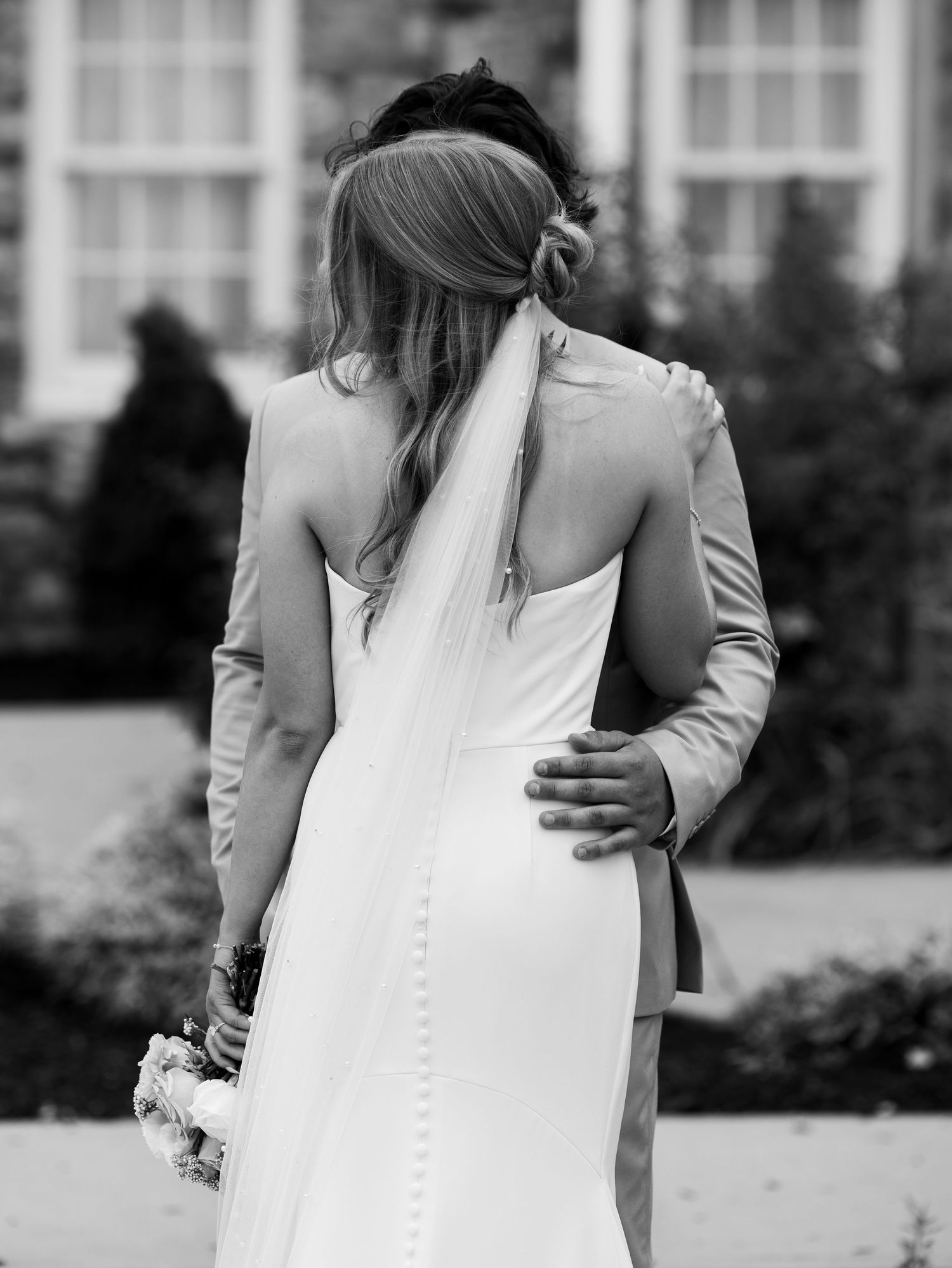 Black and white photo of a bride and groom sharing a romantic moment in a lush, tree-lined garden.