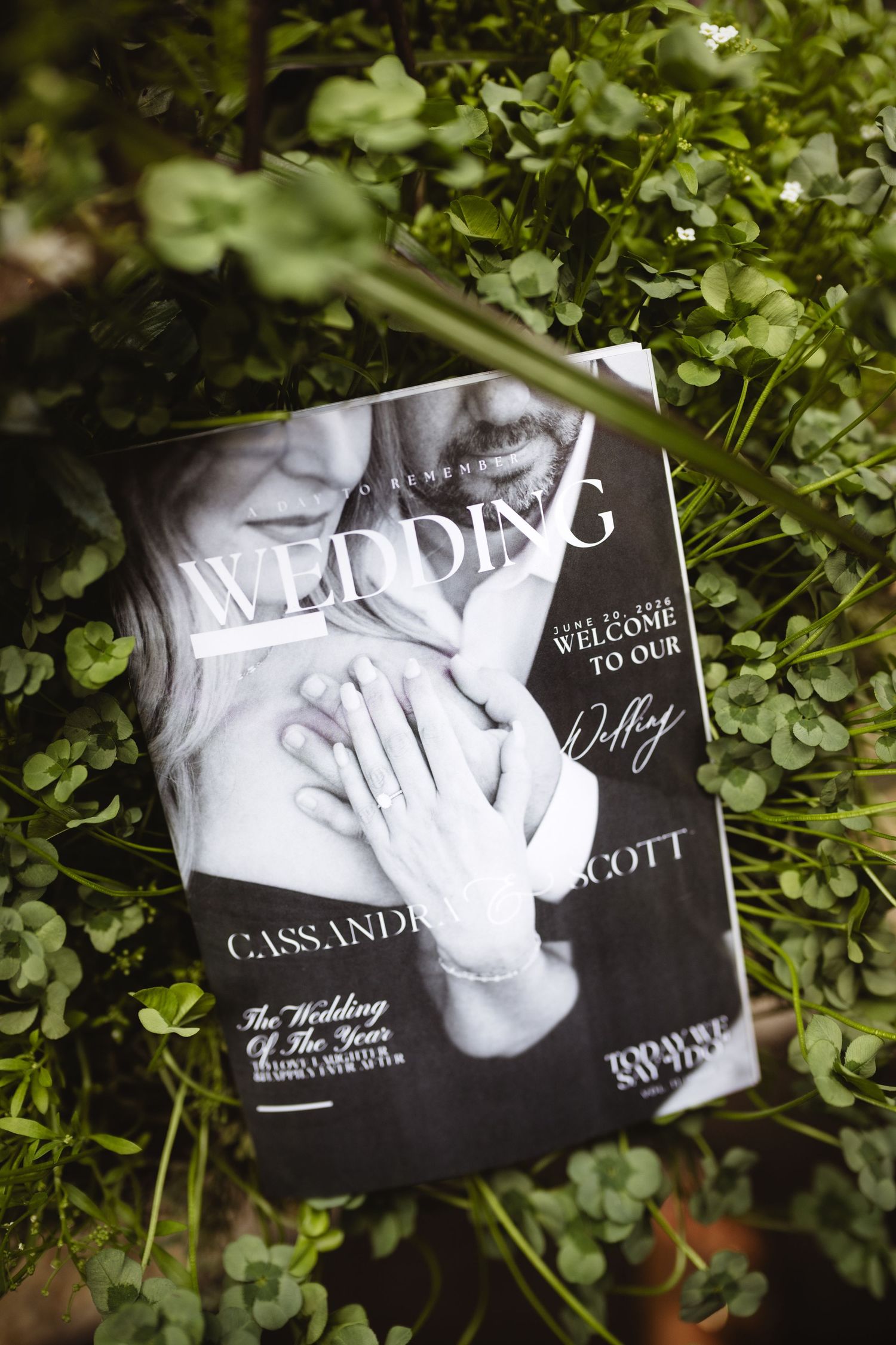 Black and white wedding magazine program for Cassandra and Scott resting on lush green clover leaves.