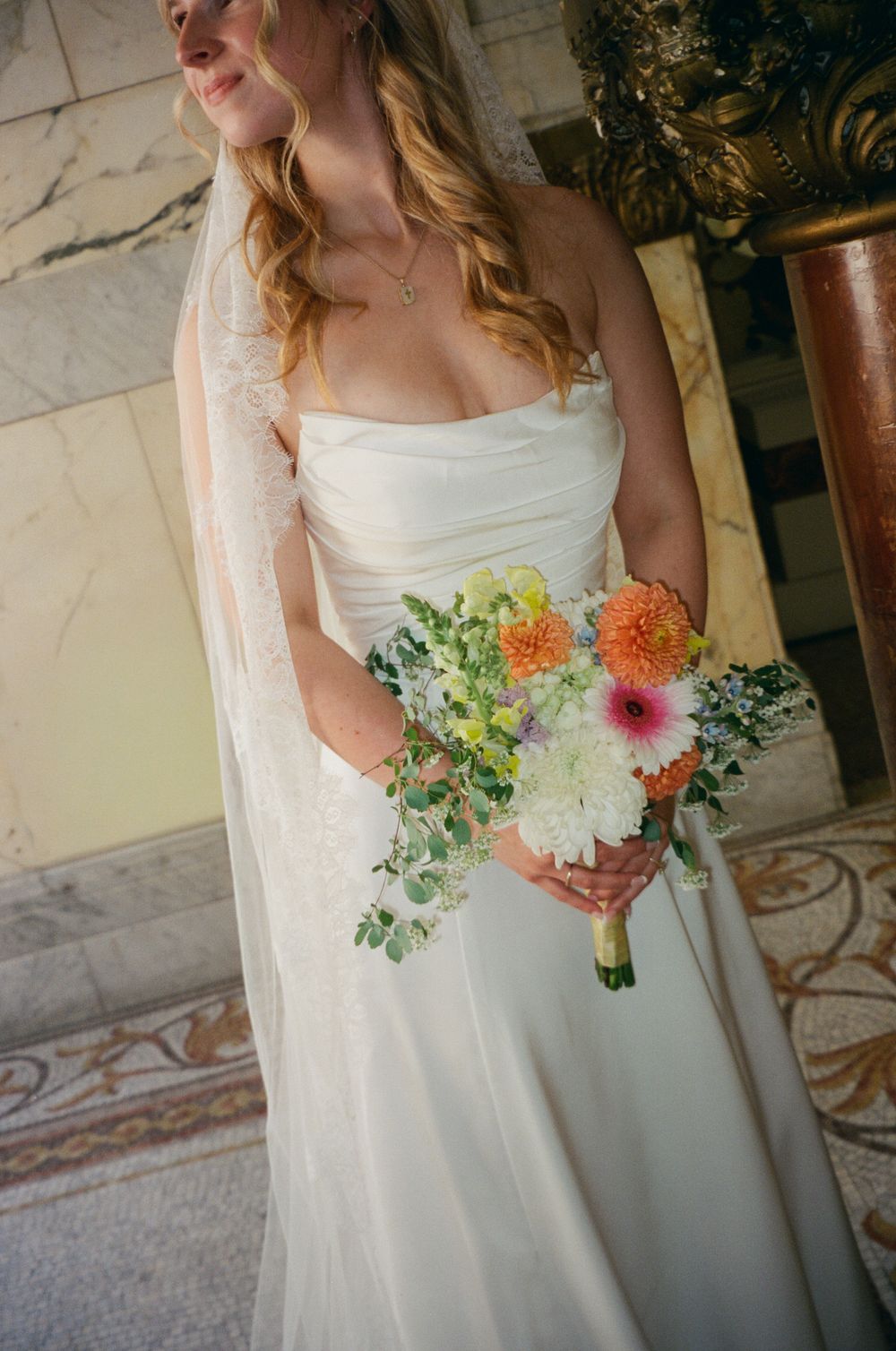 Close-up of bride in strapless white gown holding a colorful bouquet of dahlias and wildflowers.