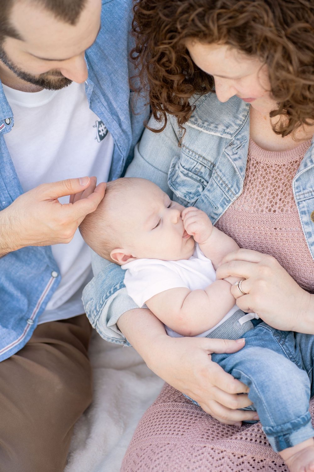 Parents lovingly gazing at their newborn baby, dressed in denim and pink, sharing a tender family moment.