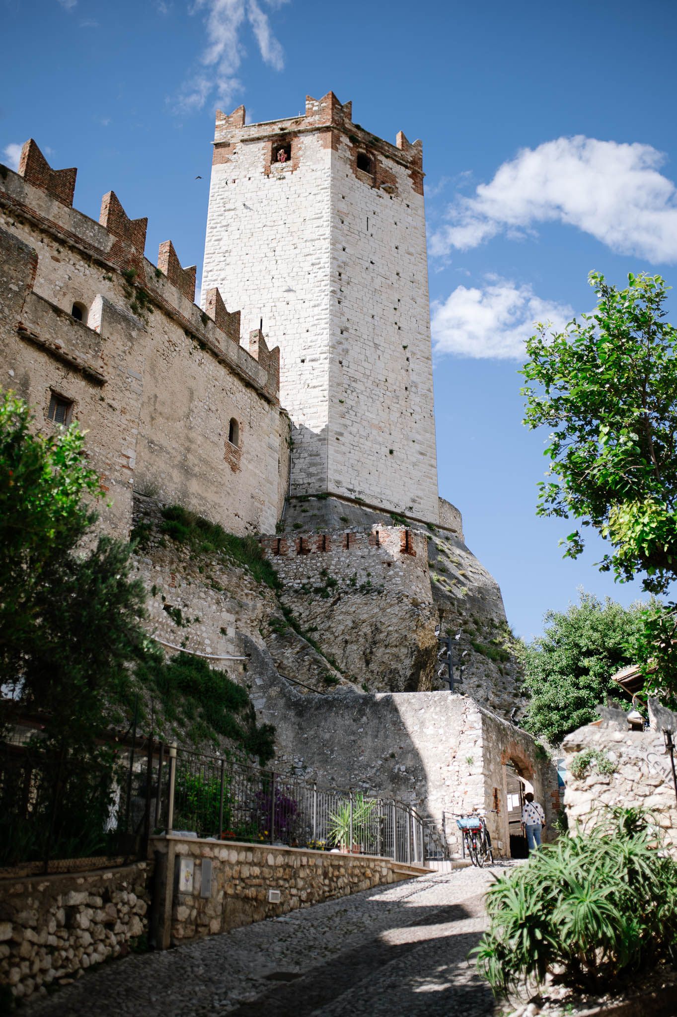 Historic medieval castle tower with white stone walls and battlements against a blue sky in Italy.
