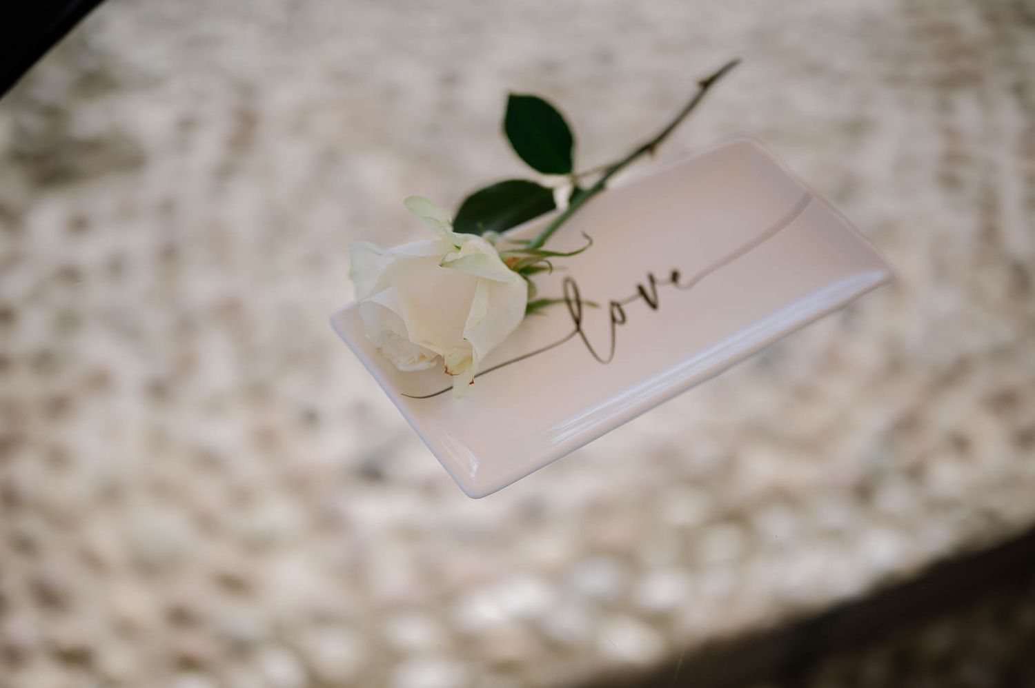 White rose resting on a love-inscribed card on a marble surface, perfect for a romantic wedding detail.