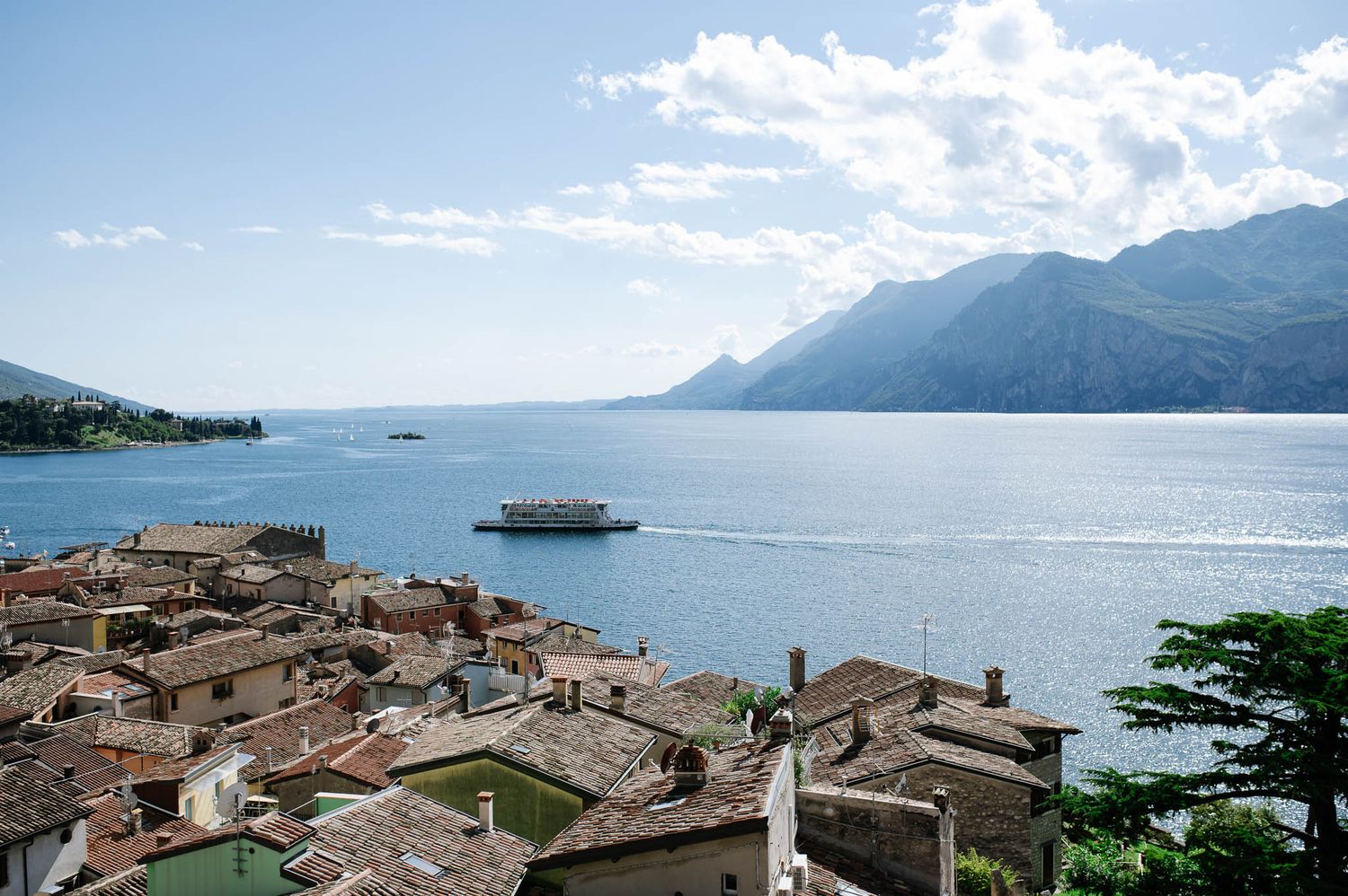 Aerial view of Malcesine village rooftops overlooking Lake Garda with mountains and a ferry in Italy.