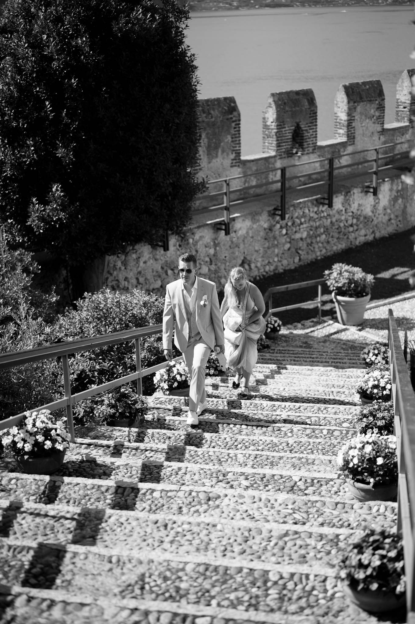Bride and groom walking down ornate stone steps flanked by flowers at a romantic castle wedding venue.