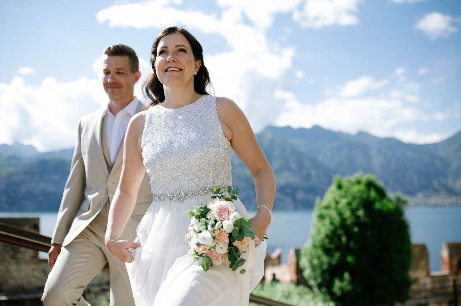 Bride and groom walking hand in hand with stunning lake and mountain views on their wedding day.
