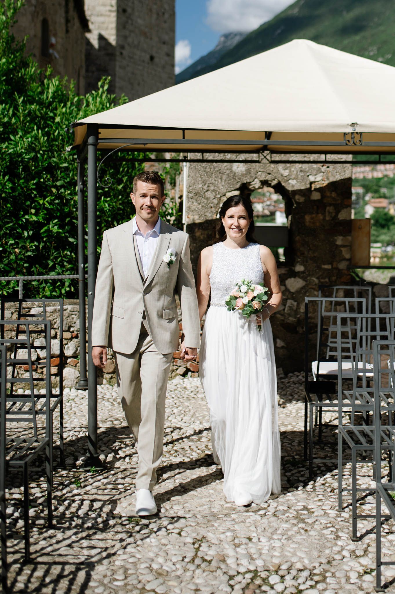 Bride and groom walk hand in hand under a gazebo at an outdoor castle wedding ceremony.