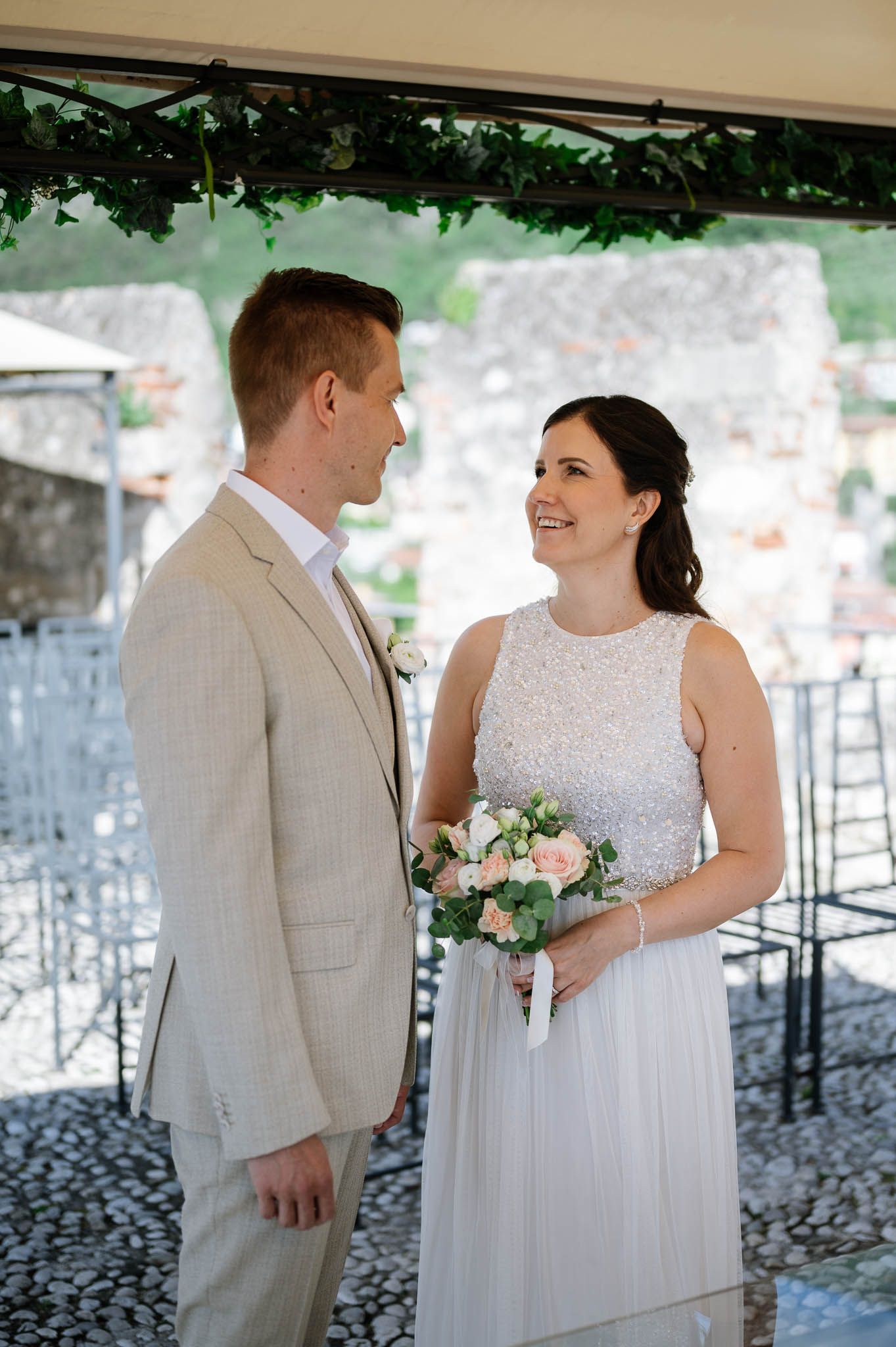 Bride and groom sharing a smile during outdoor wedding ceremony, bride holding pink and white bouquet.