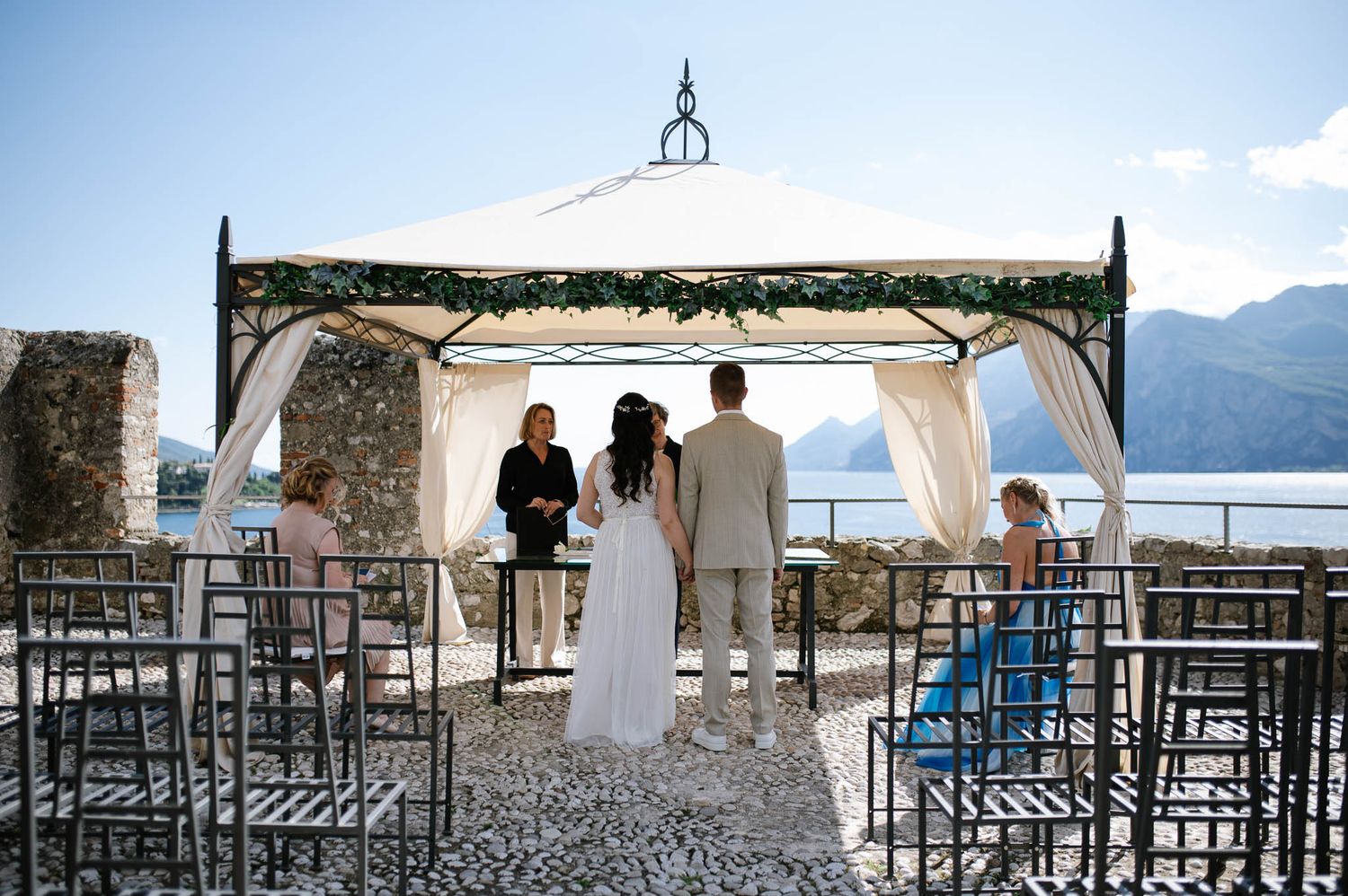 Outdoor wedding ceremony under a white gazebo at Malcesine Castle with Lake Garda backdrop.