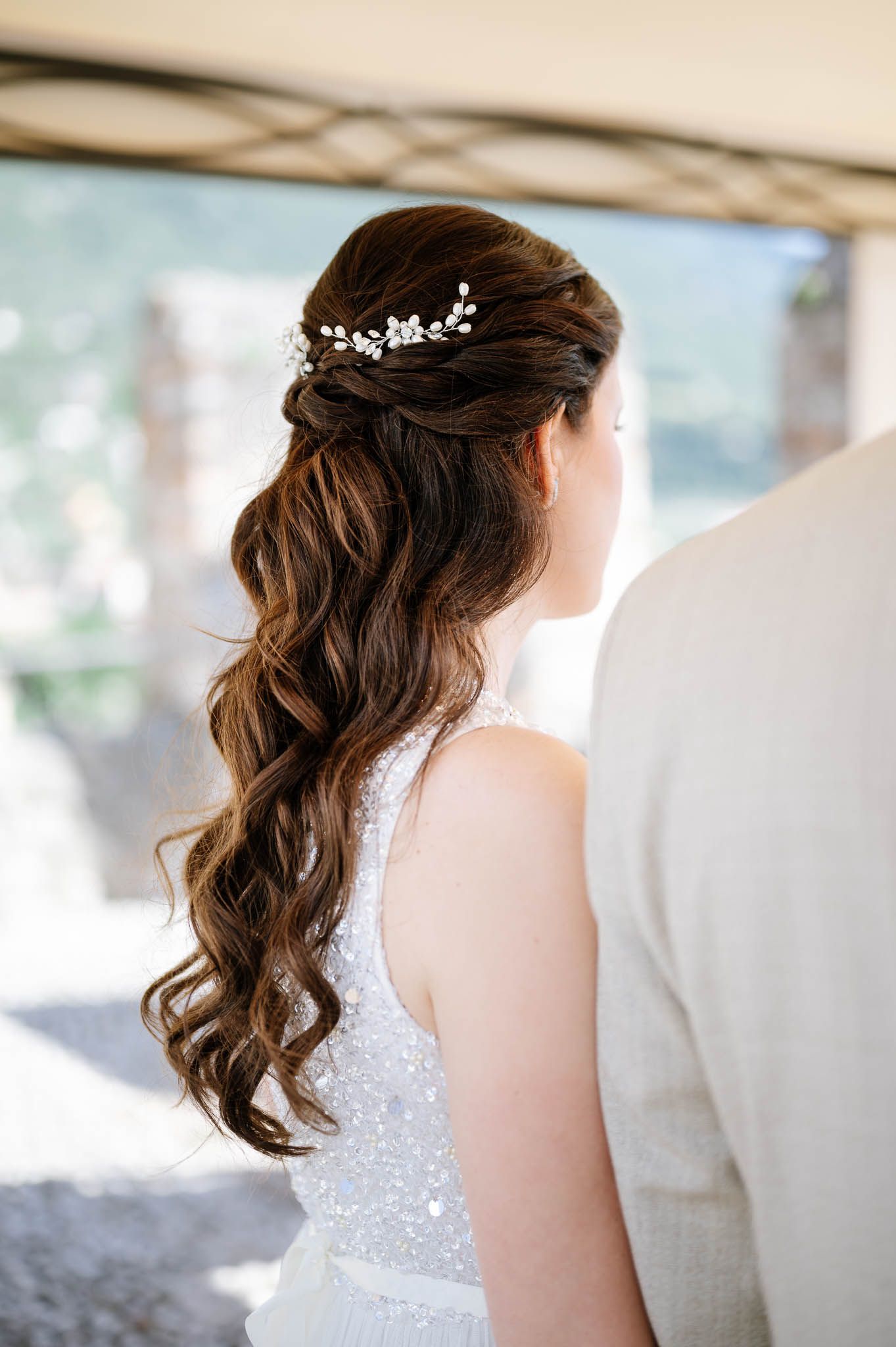 Bride with long curly brown hair adorned with a delicate floral hair vine at her wedding ceremony.