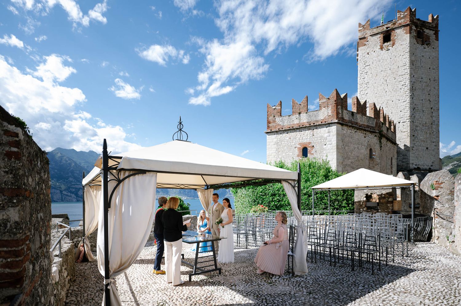 Elegant outdoor wedding ceremony setup at a historic castle with lake and mountain views.