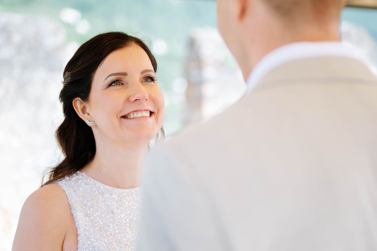 Radiant bride smiles at groom during intimate outdoor wedding ceremony in natural light.