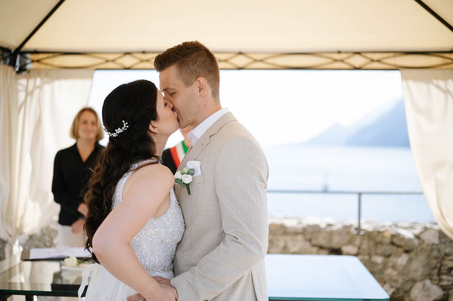 Bride and groom share their first kiss at an outdoor wedding ceremony with a scenic lake view.