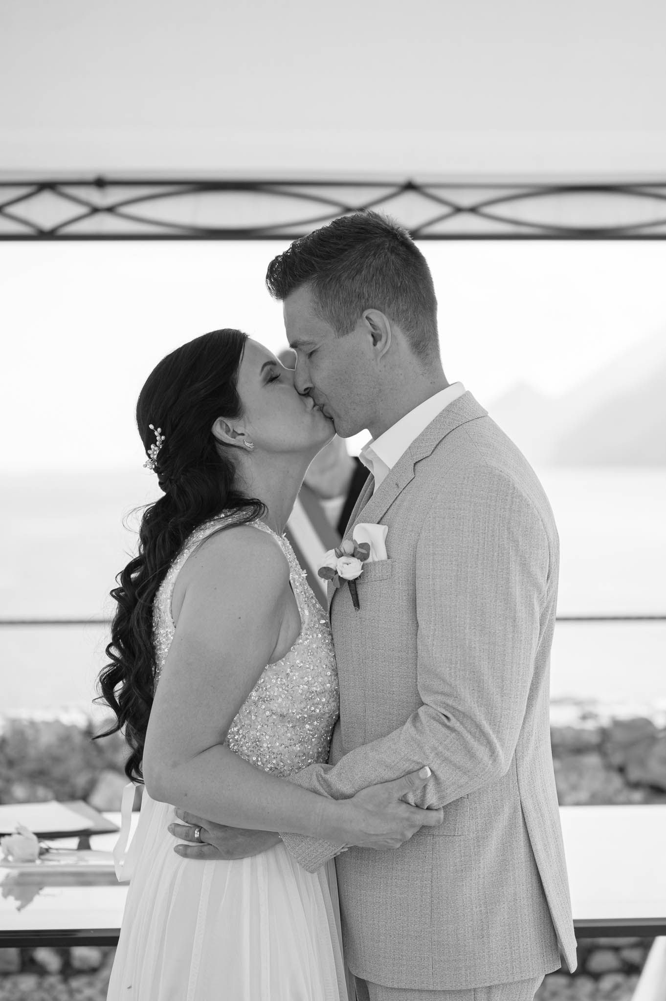 Black and white photo of a bride and groom sharing their first kiss at an outdoor wedding ceremony.