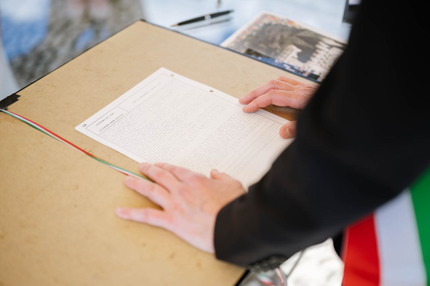 Official signing of wedding documents during a civil ceremony with Italian flag visible.