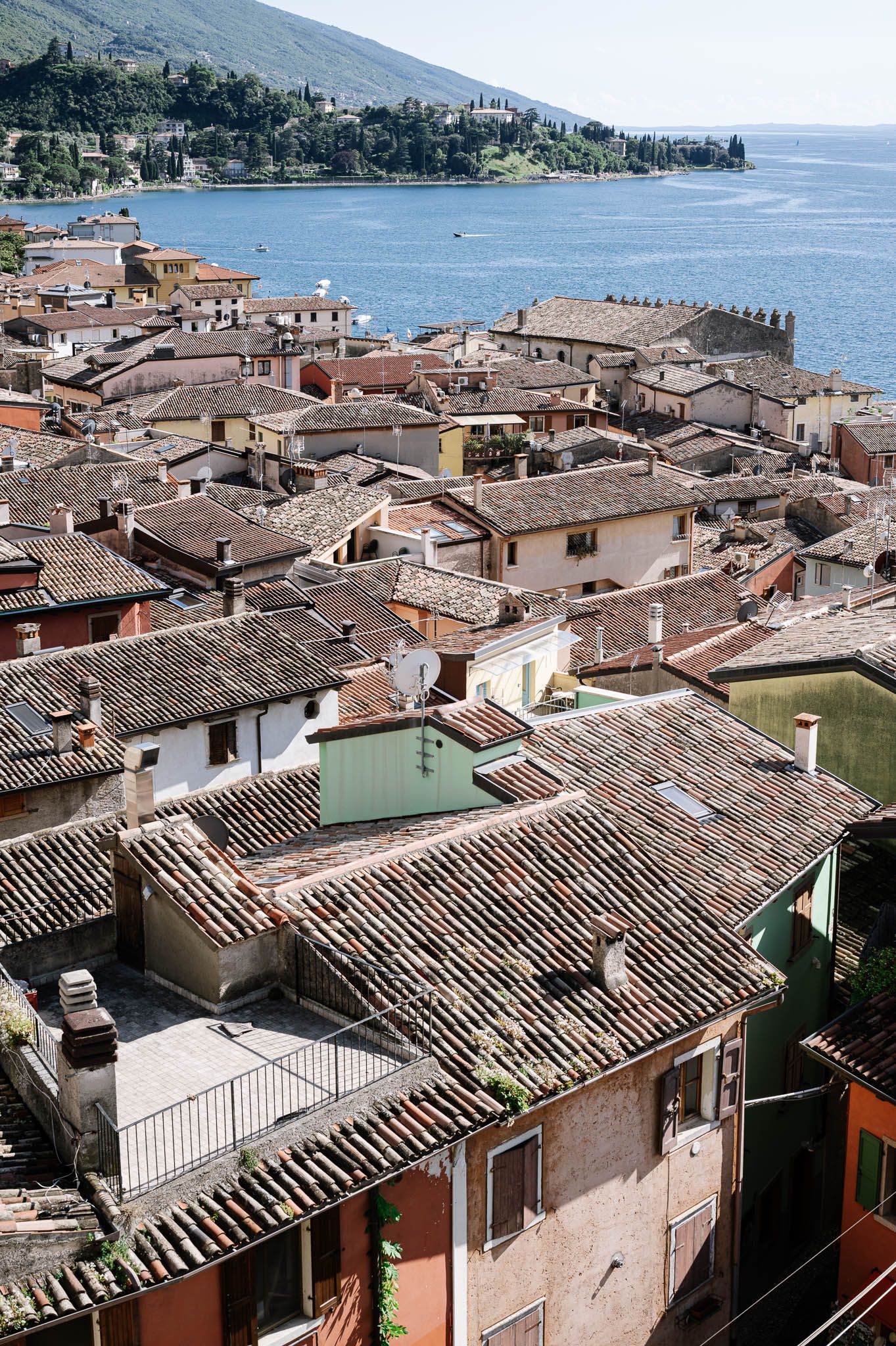 Aerial view of Italian village rooftops with terracotta tiles overlooking a serene blue lake.