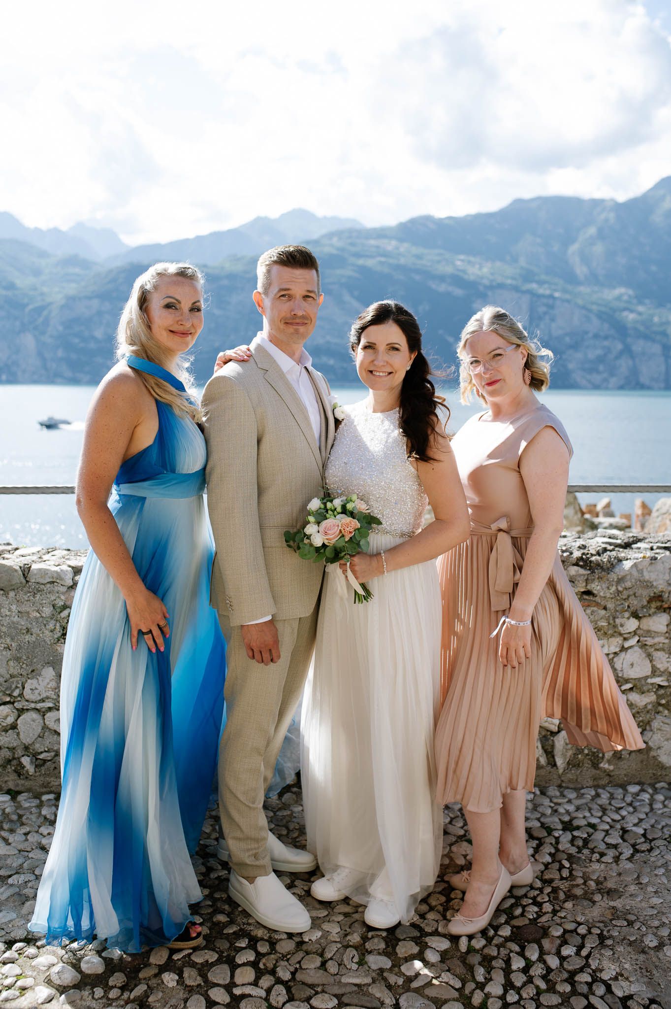 Wedding couple posing with two bridesmaids against stunning lake and mountain backdrop in Italy.