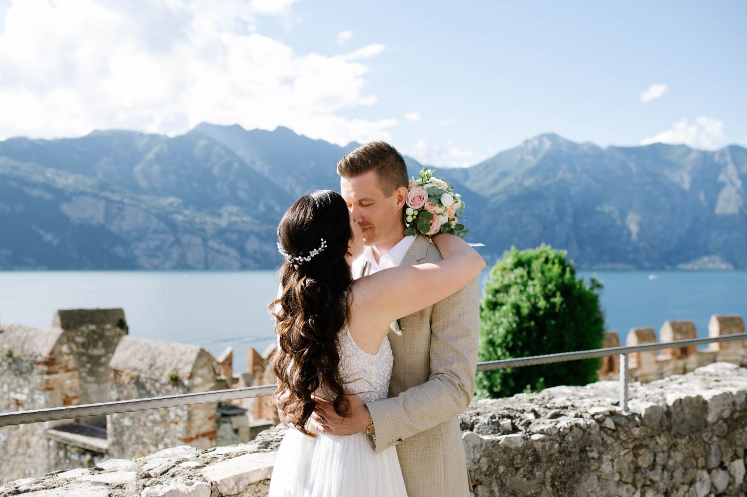 Newlyweds sharing romantic embrace with breathtaking alpine lake and mountain scenery behind them.