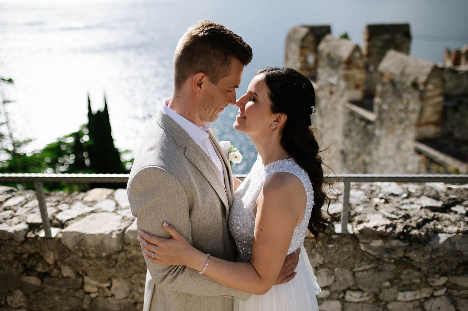 Bride and groom share a romantic embrace at a stone terrace overlooking a beautiful lake.