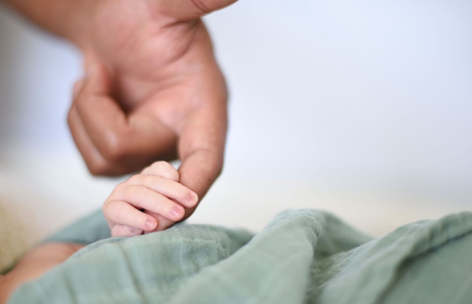 Close-up detail of tiny newborn baby toes against soft green fabric background.