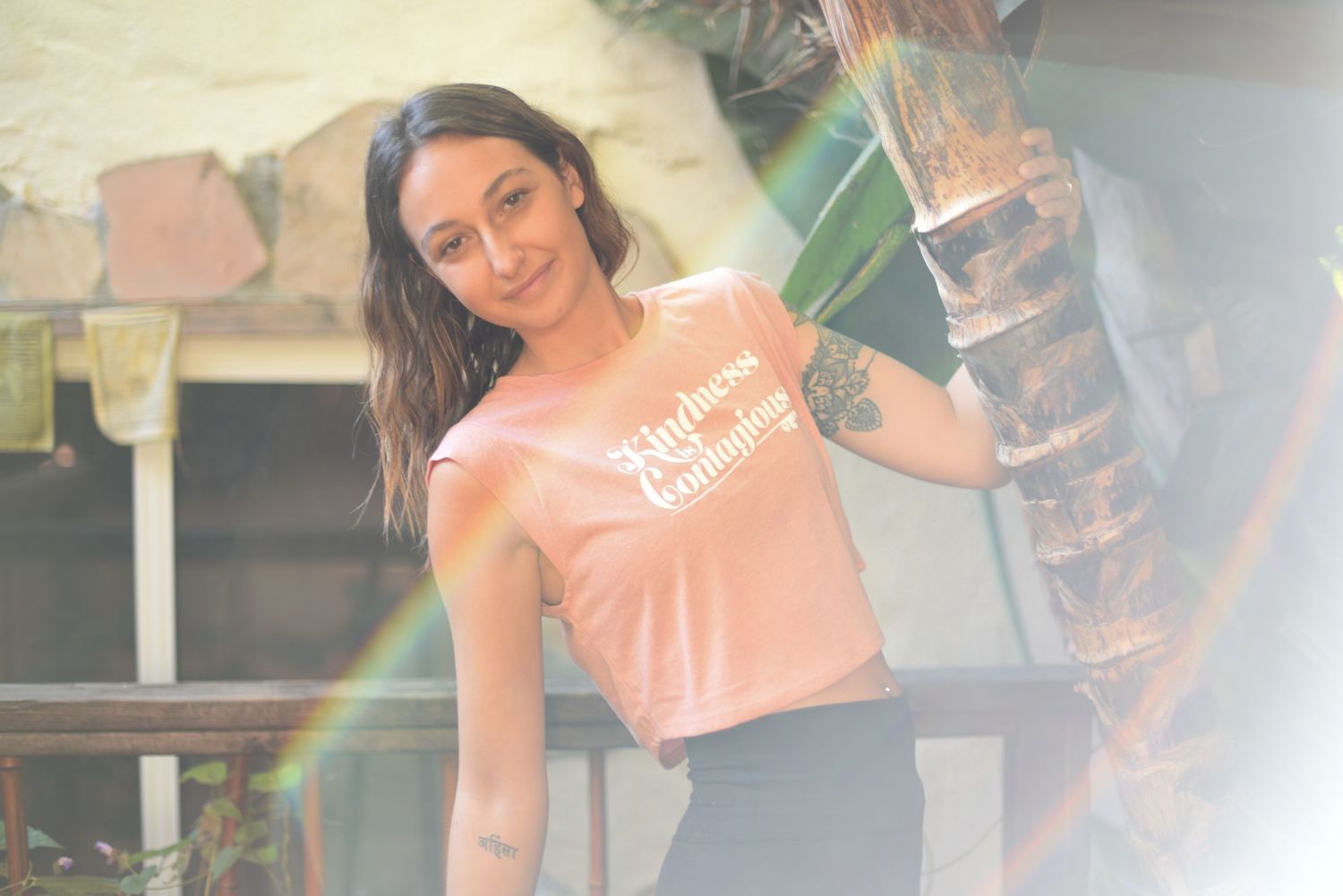 Person wearing a peach-colored crop top with text in an outdoor tropical setting.