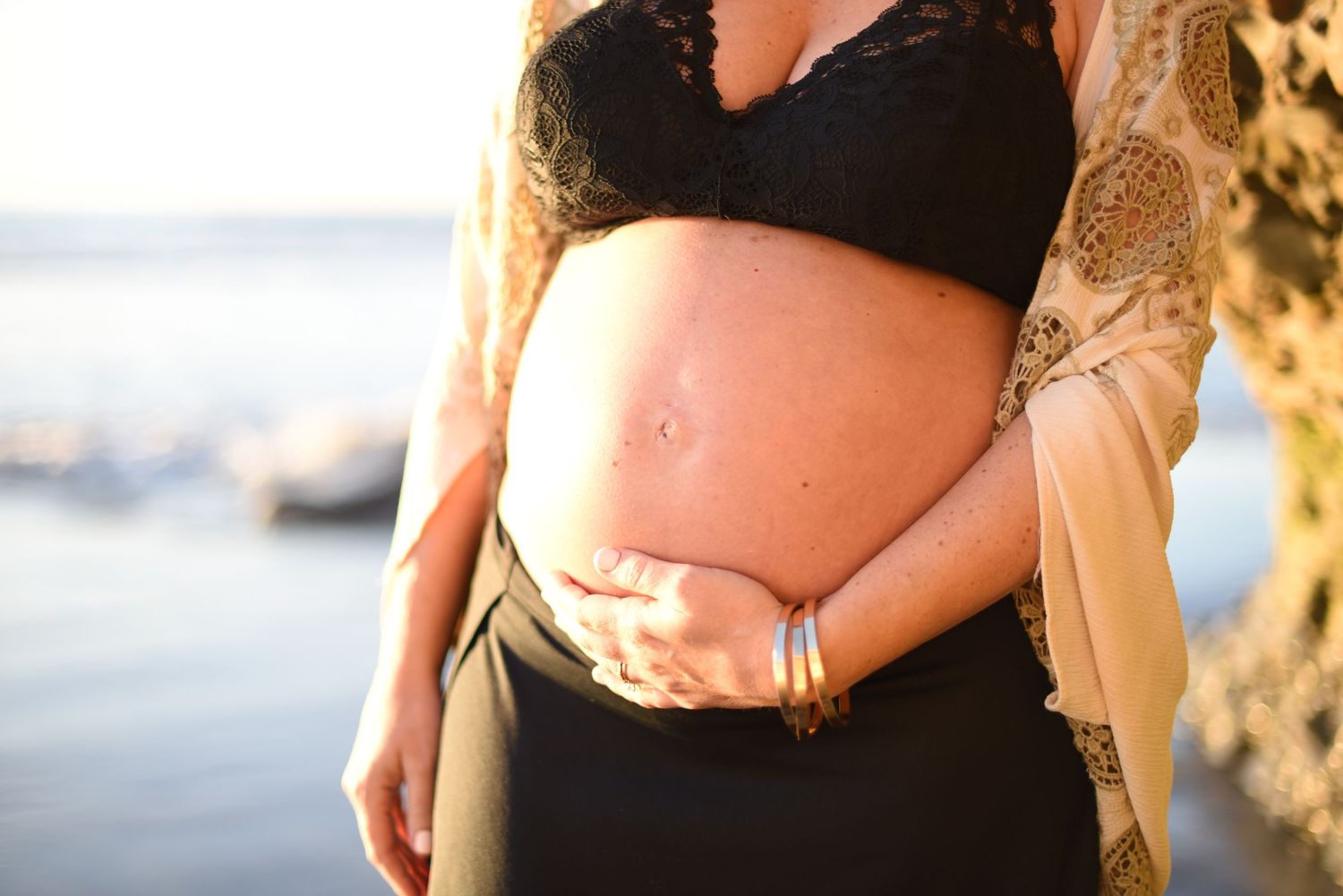 Silhouette of pregnant belly against sunset beach background.
