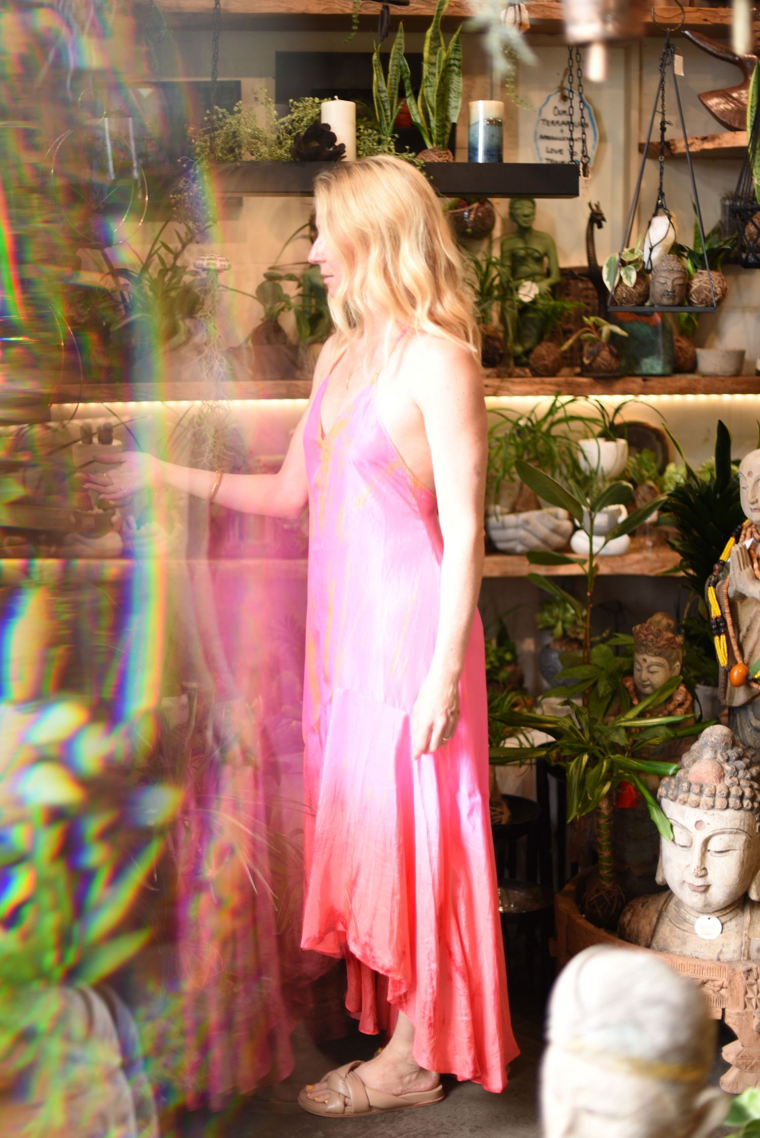 Woman in pink dress surrounded by plants and Buddha statue with prismatic light effects.