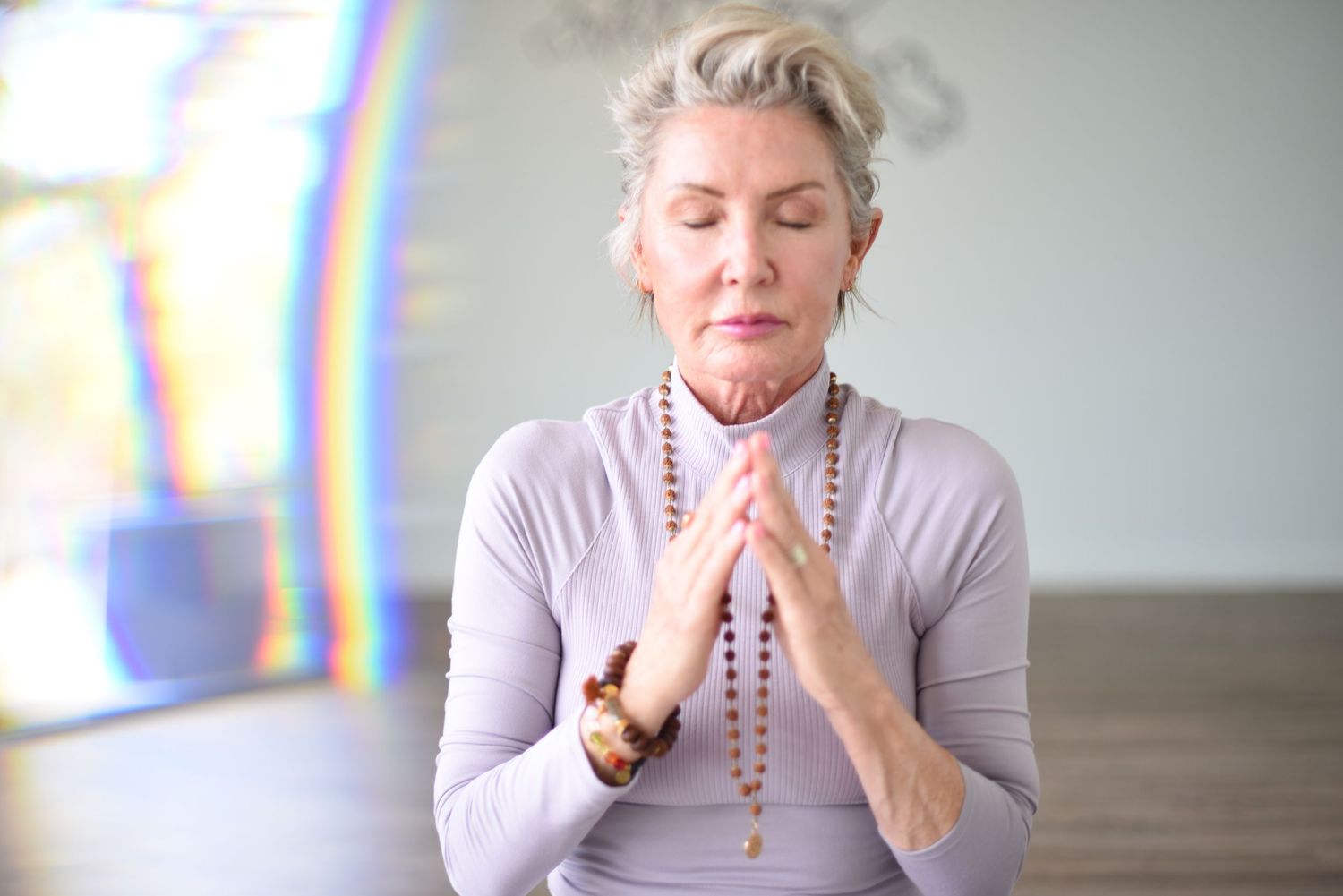 Woman meditating with prayer beads in serene setting with rainbow light effect.