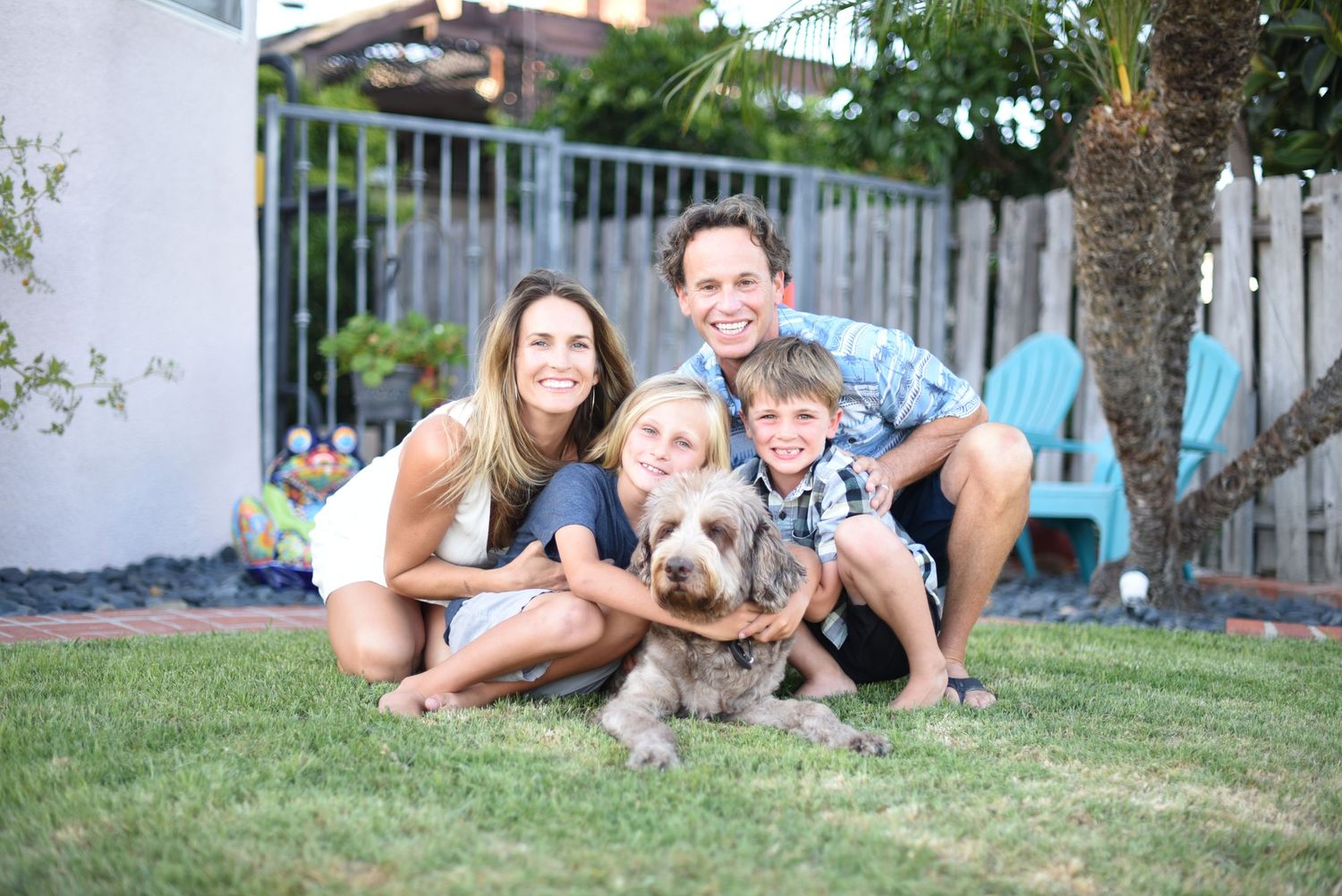 Happy family sitting on grass with their golden retriever in backyard.