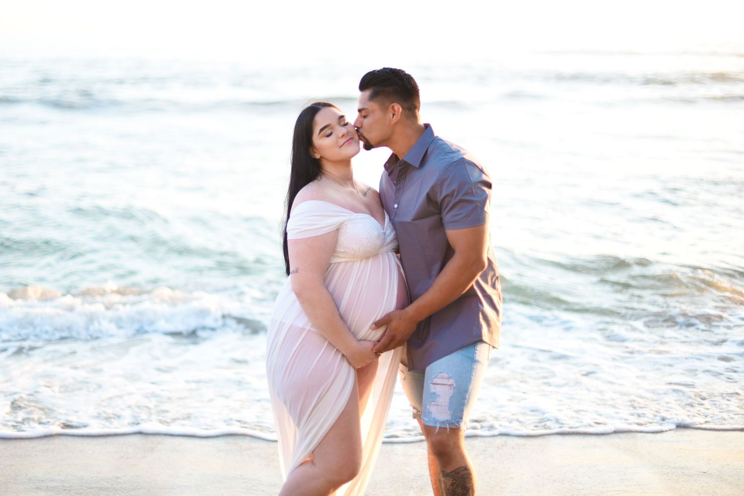 A prenatal couple embraces on iconic Windansea beach as ocean waves roll in behind them during a tender moment. Maternity.
