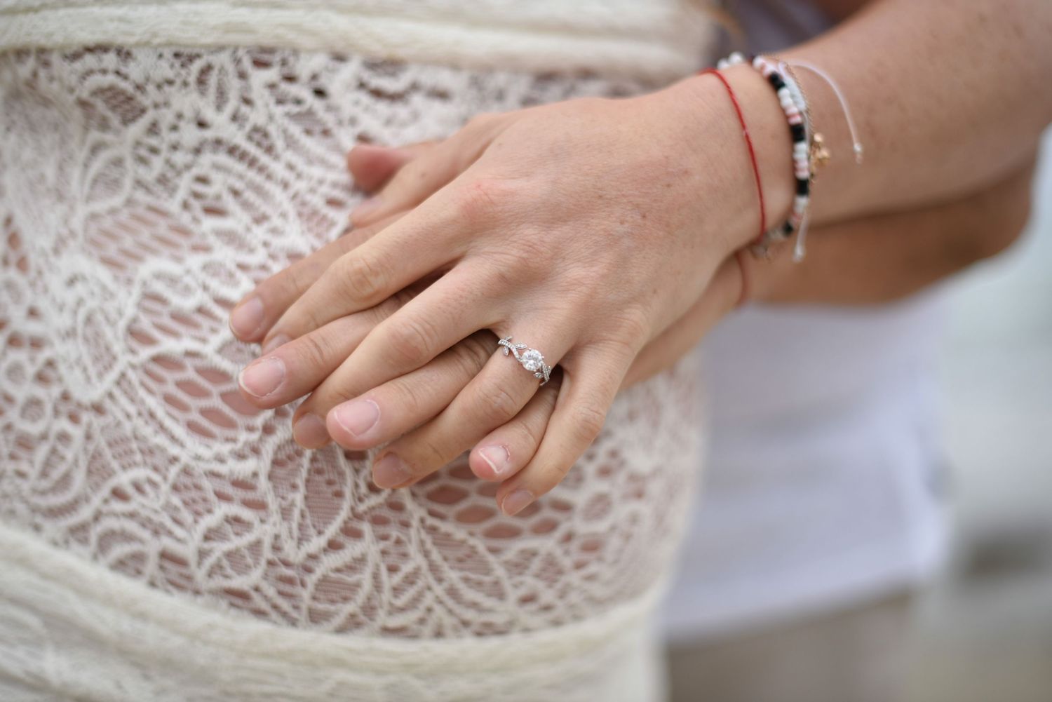 Elopement detail shot showing delicate white lace patterns with hands displaying engagement rings and mother to be.