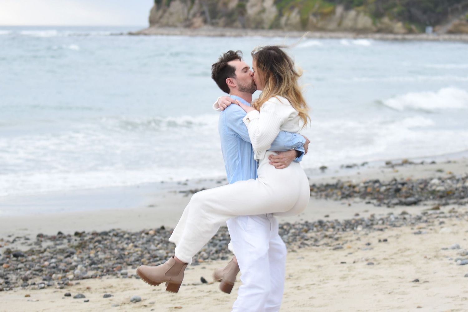 Romantic couple embraces on a rocky beach with waves and cliffs in the background. Tourmaline Beach. Pacific Beach, California.