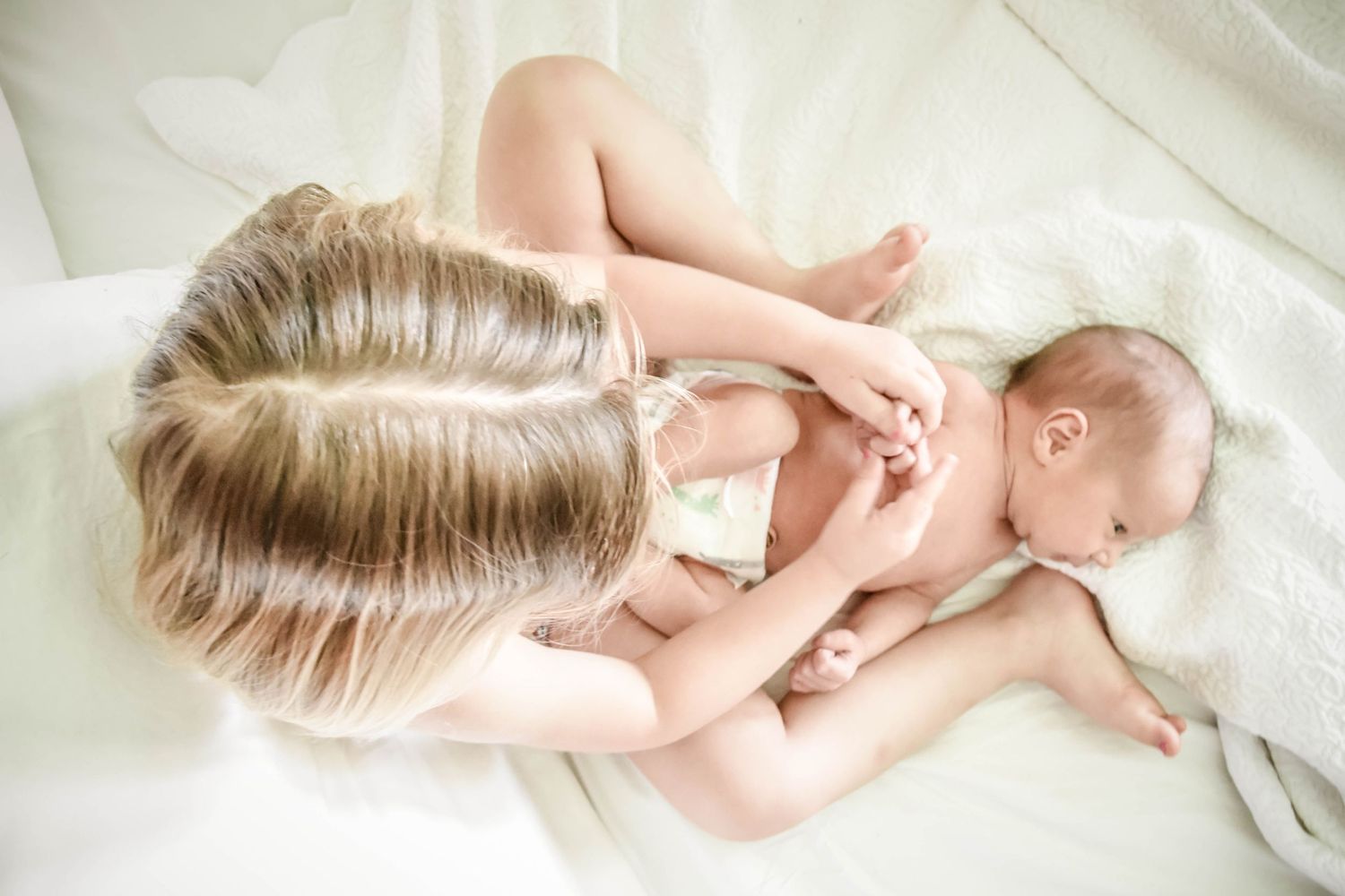 Tender moment between mother and baby on white bedding.