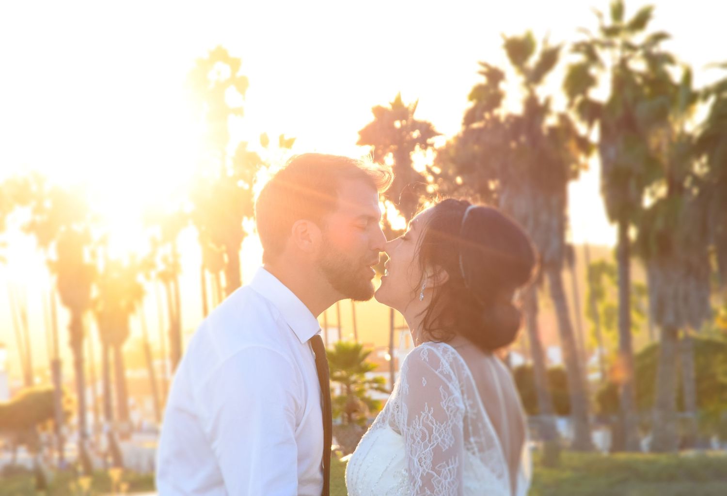 Wedding couple silhouetted against palm trees during golden hour sunset.