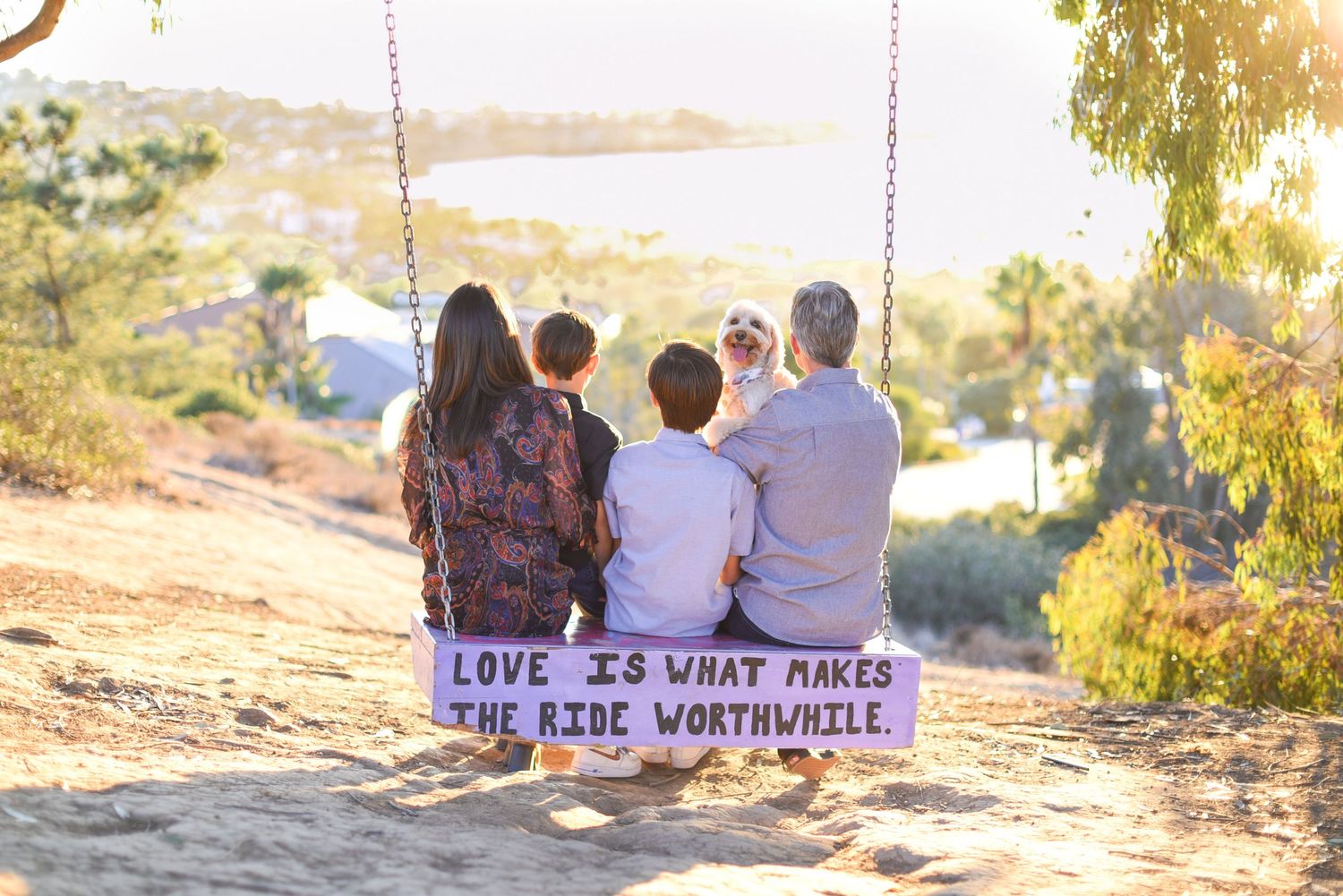 Family sitting together on swing with inspirational quote about love against scenic sunset view.