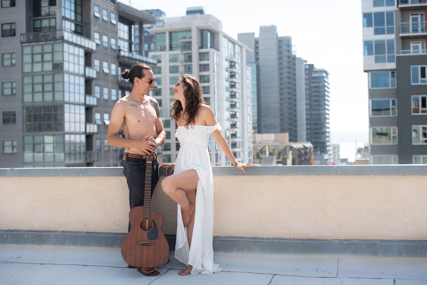 A couple shares a romantic moment on a rooftop terrace with a guitar and city skyline in the background.
