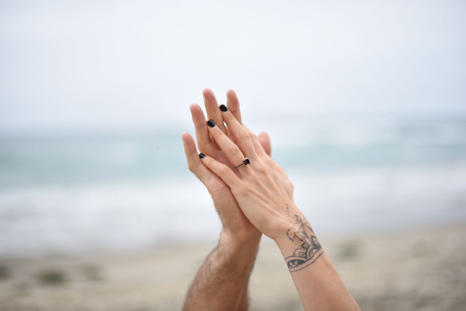 Two hands raised against a misty beach background with one hand showing her black diamond engagement ring.