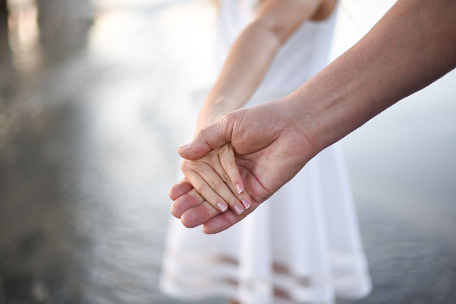 Father, daughter. Two hands hold a glowing wooden cross in a soft defocused background, creating a spiritual atmosphere.
