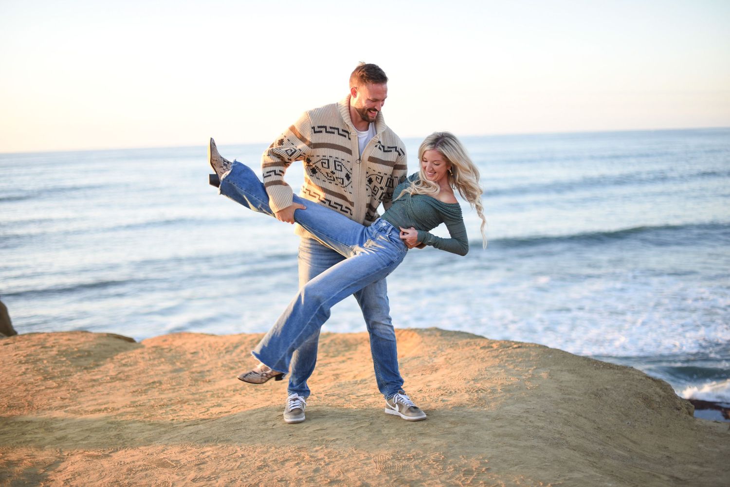 Playful couple enjoying a sunset moment on a rocky cliff overlooking the ocean waves. Sunset Cliffs. Point Loma. Ocean Beach. San Diego.