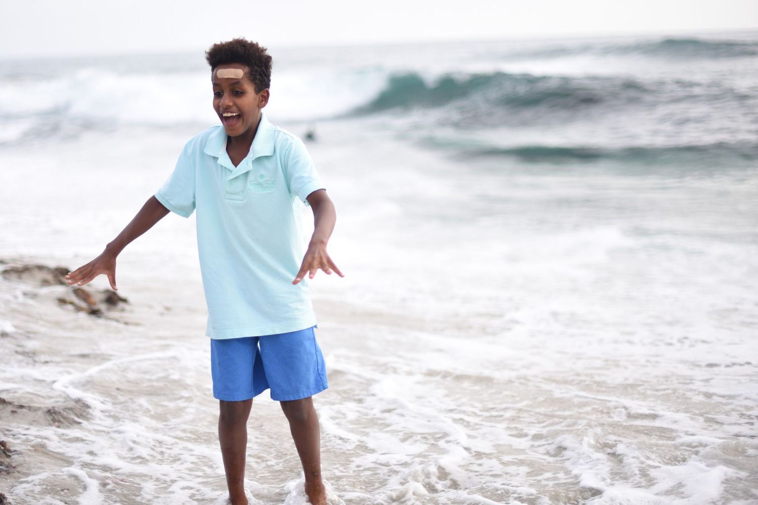 Young child playing and jumping joyfully on a sunny beach with ocean waves in the background.