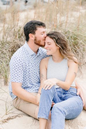 Happy newly engaged couple on Jekyll Island beach during surprise engagement photos, couple sitting in sand