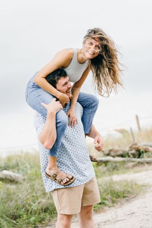 Couple goofing around at Driftwood beach during a surprise portrait session, she's on his shoulders after they got engaged