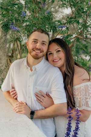Couple snuggled by the Crane Cottage of Jekyll Island behind them, during an engagement photography session portraits in Golden Isles, GA