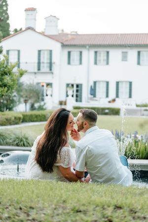 Couple sitting with the Crane Cottage of Jekyll Island behind them, during an engagement photography session portraits in Southeastern GA